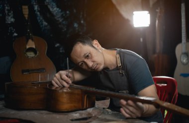 Gitar yapımcıları Asyalı adam laboratuarda akustik gitar yapıyor. Asyalı gitarcı, müzisyenler için el yapımı gitar dükkanı inşa ediyor. İnce ahşap işçiliği, gelenek, antik el sanatları.