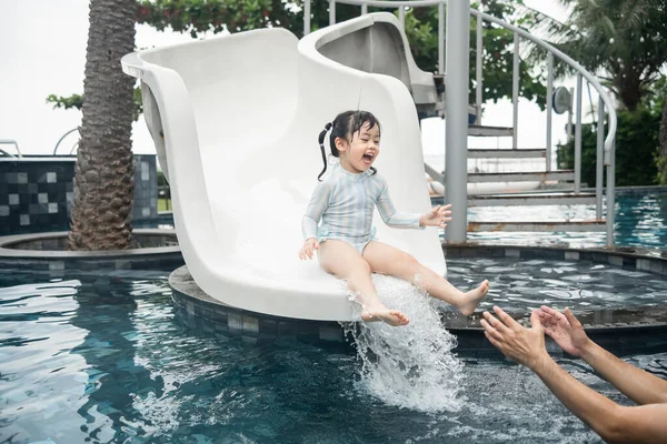 Asian father and daughter swimming playing slide pool in the pool at the resort, smiling and laughing. Having fun in the pool at the resort hotel, family happy concept.