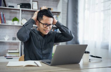 Asyalı serbest çalışan adam gözlük takıyor ve evde dizüstü bilgisayarla çalışırken stresli depresyon dönemleri geçiriyor. Depresyondaki adam evde çalışan üzgün adamlar. Herhangi bir yerde çalışma kavramı.
