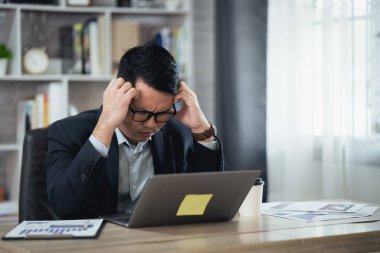 Asyalı iş adamı gözlük takıyor ve evde dizüstü bilgisayarla çalışırken stresli depresyon geçiriyor. Depresyondaki adam evde çalışan üzgün adamlar. Herhangi bir yerde çalışma kavramı.