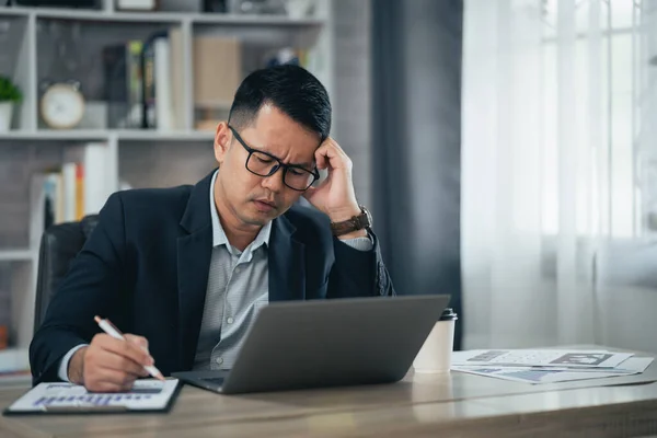 アジアのビジネスマンは 自宅のノートパソコンで仕事をしながら ストレスの多いうつ病悲しい時間を過ごしています うつ病の男は自宅から働く悲しいシリーズ どこにいても — ストック写真