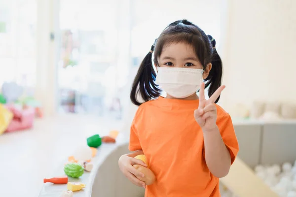 Азиатская Девушка Поднимает Два Пальца Знак Носить Хирургическую Маску Играть — стоковое фото
