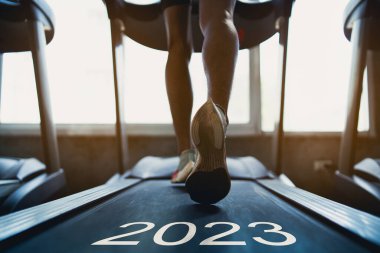 Mutlu yıllar 2023.2023 yeni yılın başlangıcını simgeliyor. Ayaklarını kapat, spor koşucusu fitness kulübünde koşu bandında koşuyor. Kardiyo çalışması. Sağlıklı yaşam tarzı, spor salonunda erkek eğitimi..