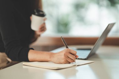 Asian freelance woman smiling holding cup of hot coffee and working on laptop computer on wooden table at home. Entrepreneur woman working for her business at home. Business work at home concept.