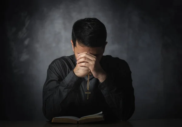 Religious asian man praying holding necklace of crosses and bible verses praying for holy blessings sitting on the table gray background. Spirituality and religion. Christian prayer religion concept.