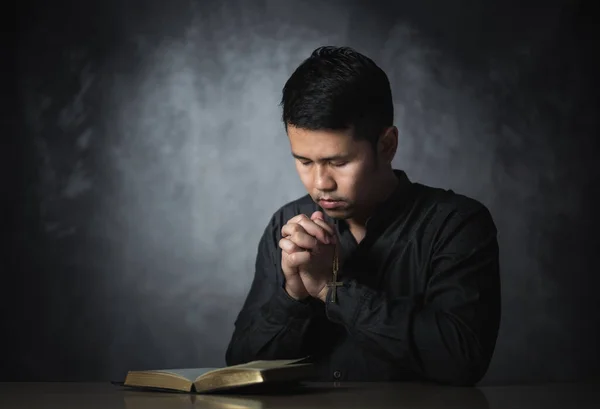 Religious asian man praying holding necklace of crosses and bible verses praying for holy blessings sitting on the table gray background. Spirituality and religion. Christian prayer religion concept.