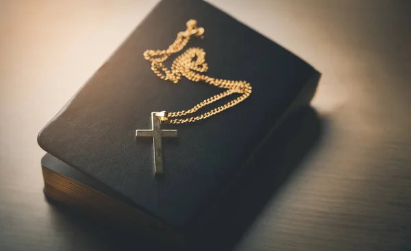 Close up top view Christian gold stainless steel crucifix necklace crosses placed on bible black leather cover place on a wooden table. Spirituality and religion. Christian prayer religion concept.