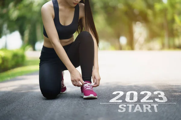 Sport woman runner tie shoelaces start into the new year 2023. Start up of runner woman running on nature race track go to Goal of Success. People running as part of Number 2023. Sport health care.