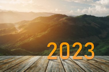Mutlu yıllar 2023.2023 yeni yılın başlangıcını simgeliyor. Mektup 2023 'te ahşap masa terasında başlıyor günbatımı dağ manzarası çevre ekolojisi veya yeşil duvar kağıdı konsepti.