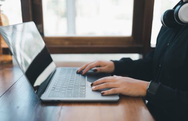 İşletme serbest girişimcisi beyaz kulaklıklı bir kadının elleri dizüstü bilgisayarda klavye ve kafe kahve dükkanındaki ahşap masada çalışıyor. İş teknolojisi kavramı.