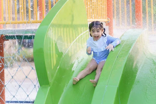 亚洲可爱的女婴开心地笑着 在度假胜地的游泳池里玩滑水池 在度假酒店的游泳池里玩乐 享受家庭快乐的概念 免版税图库图片