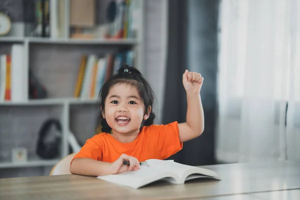 Asian baby kid girl holding magnifying glass and raise your hand reading book education, children and school concept - happy smiling student girl learning studying. Education development concept.