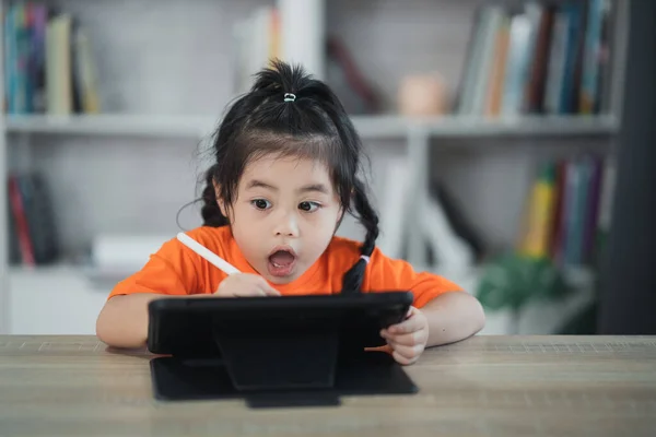 Asian girl use digital pen and touch on screen tablet screen attentively. overstimulated children concept. Too much screen time. Cute girl watching videos while tv, Internet addiction concept.