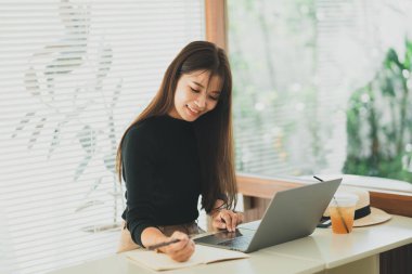 Akıllı gündelik giyinen Asyalı genç bir kadın yaratıcı ofiste ya da kafede otururken dizüstü bilgisayarla çalışıyor. Kafedeki ahşap masada dizüstü bilgisayarla çalışan genç bir kız.