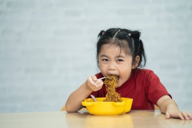 Asyalı kız bebek çatal ve kaşıkla yemek masasında lezzetli erişte yemekten zevk alıyor. Mutlu Asyalı bebek yemek masasında tek başına yemek yeme alıştırması yapıyor. Bebek maması konsepti