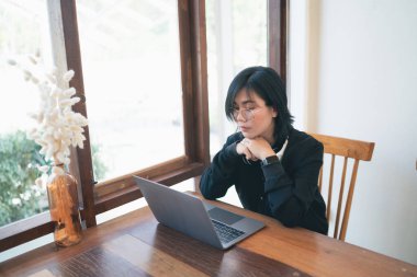 Beyaz kulaklıklı, klavyesini bilgisayarda ve kafeteryadaki ahşap masada yazan serbest girişimci bir kadın. İş teknolojisi kavramı.