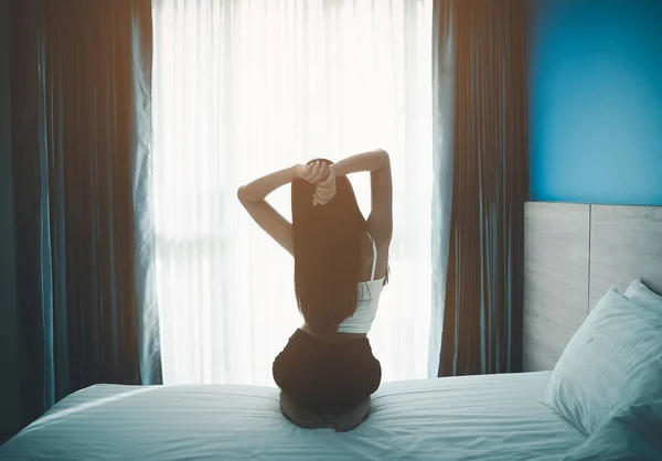 若いアジアの女性は 寝室のインテリアでベッドの上で窓やストレッチ腕を見て幸せなリラックスして目を覚ます 居心地の良い寝室で朝早く起きて — ストック写真