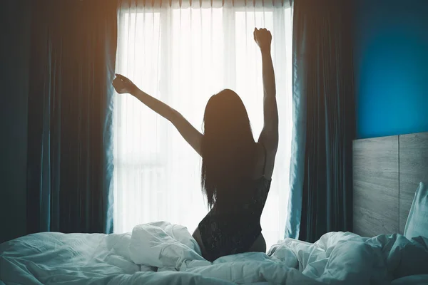 若いアジアの女性は 寝室のインテリアでベッドの上で窓やストレッチ腕を見て幸せなリラックスして目を覚ます 居心地の良い寝室で朝早く起きて — ストック写真