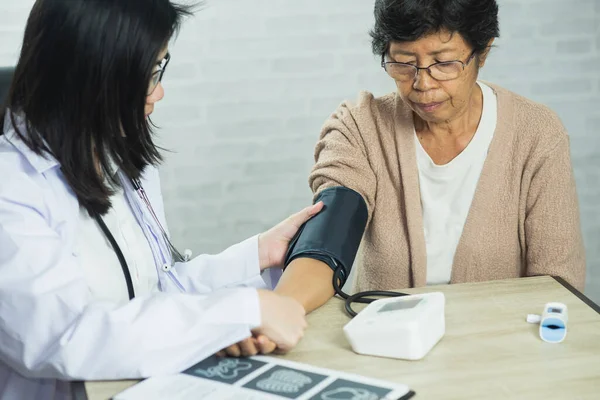 stock image Woman doctor measuring blood pressure for elderly female patient on the doctor's office desk. Elderly female patient suffering from hypertension Checking for sickness in hospital. Health check up.