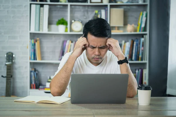 アジアのビジネスマンは 自宅のノートパソコンで仕事をしながら ストレスの多いうつ病悲しい時間を過ごしています うつ病の男は自宅から働く悲しいシリーズ どこにいても — ストック写真