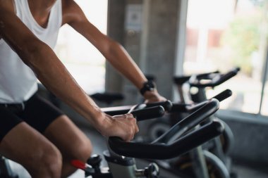 Spor salonunda bisiklet üzerinde egzersiz yapan Asyalı sporcunun ellerini kapat. Kardiyo yapma azmi onu sağlıklı kılıyor. Egzersiz bisikleti sporu konsepti.
