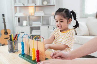 Genç tatlı Asyalı kız ve anne babası abaküsü renkli boncuklarla öğreniyorlar evdeki oturma odasında kanepe saymayı öğrenmek için. Çocuk bebek gelişimi konsepti.