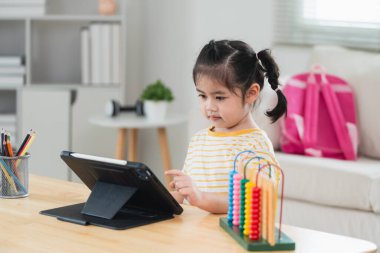 Asyalı kız tablet ekranına dikkatlice bakıyor ve dokunuyor. aşırı uyarılmış çocuk konsepti. Çok fazla ekran zamanı. TV ve internet bağımlılığı konsepti izlerken güzel bir kız video izliyor..