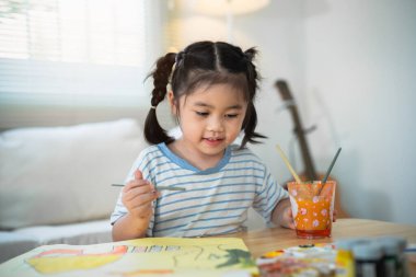 Suluboya kullanarak renkli resimlerle gülümseyen sevimli Asyalı bebek. Boyalı fırça rengini kullanan Asyalı bir kız. Bebek aktivitesi yaşam tarzı konsepti.