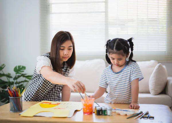 Cute little child painting with colorful paints. Asian girl and mother using crayon drawing color. Daughter and mom doing homework coloring cartoon characters. Baby artist activity lifestyle concept.