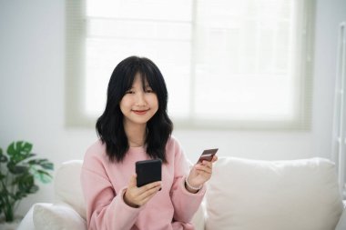 İnternetten alışveriş yapmak için cep telefonu akıllı telefonu kullanan bir kadın. Evde çalışan Asyalı kadın. Çevrimiçi alışveriş, e-ticaret, internet bankacılığı, harcama, ev konseptinden çalışma.