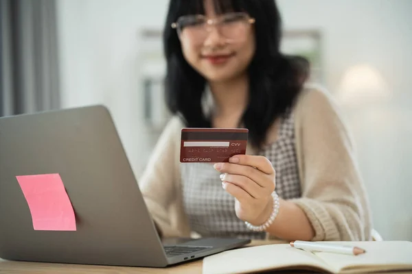 Woman holding showing credit card to shopping online. asian woman working at home. Online shopping, e-commerce, internet banking, spending money, working from home concept.