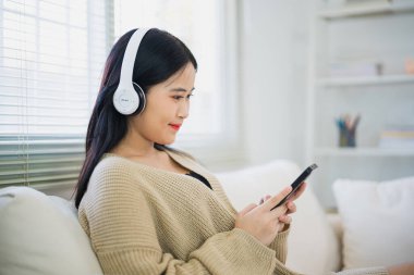 Asyalı serbest kadın gülümseyerek uzanıyor rahatlıyor, cep telefonu kullanıyor ve kulaklık takıyor kanepede müzik dinliyor. Girişimci kadın iş arıyor, hisse senedi ticareti yapıyor ya da internet oturma odasını karıştırıyor..