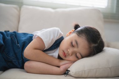 Evdeki oturma odasında yumuşak yastıklarla kanepede uyuyan tatlı küçük kız çocuğu. Kanepede uzanmış küçük bir kız..