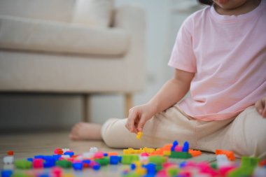 Kapatın. Neşeli Asyalı kız mutlu ve gülümsüyor renkli Lego oyuncakları oynuyor, oturma odasında yerde oturuyor, yaratıcı bir şekilde Lego ile oynuyor, renkli yapılar inşa ediyor yaratıcılığı hayal edin..
