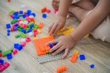 Üst Manzara. Neşeli Asyalı kız mutlu ve gülümsüyor renkli Lego oyuncakları oynuyor, oturma odasında yerde oturuyor, yaratıcı bir şekilde Lego ile oynuyor, renkli yapılar inşa ediyor yaratıcılığı hayal edin..