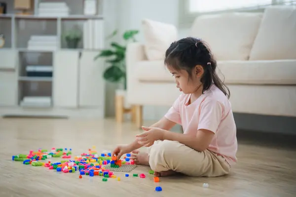 stock image Joyful Asian girl happy and smiling playing colorful Lego toys, sitting on the living room floor, creatively playing with Lego, building colorful structures creativity imagine. Learning education.