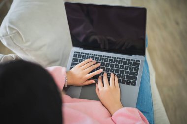 Üst Manzara. Asyalı serbest çalışan kadın gülümseyerek uzanıyor rahatlıyor, klavyede daktilo yazıyor ve dizüstü bilgisayarla kanepenin üzerinde çalışıyor. Girişimci kadın iş için oturma odasında çalışıyor. İş yeri ev kavramı.