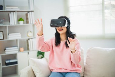 Asyalı kadın gülümsüyor ve VR oyunu oynuyor, evdeki oturma odasında eğlenmek için 3 boyutlu yenilik gözlükleri, tatilde evde neşeli Asyalı kadın. Mutlu kadın metaverse VR teknoloji konsepti oynuyor.