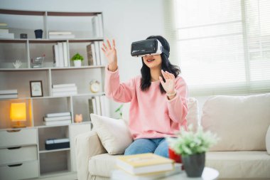 Asyalı kadın gülümsüyor ve VR oyunu oynuyor, evdeki oturma odasında eğlenmek için 3 boyutlu yenilik gözlükleri, tatilde evde neşeli Asyalı kadın. Mutlu kadın metaverse VR teknoloji konsepti oynuyor.