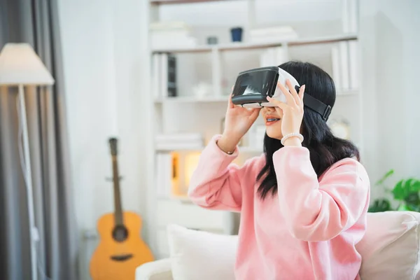 Asian woman smile and play VR game, 3D divice new innovation glasses for entertain in living room at home, asian woman joyful in house on holiday. Happy woman playing metaverse VR technology concept.