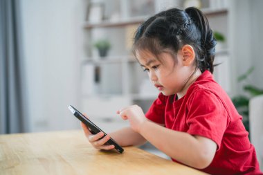 Cep telefonu ekranını kullanan ve dokunan Asyalı bir kız çocuğu. Bebek gülümsemesi cep telefonu kullanmak için komik bir zaman. Çok fazla ekran zamanı. Oturma odasında televizyon seyreden tatlı bir kız, internet bağımlılığı..