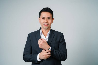 Asyalı iş adamı takım elbiseli, gri arka planda yalnız duran kamera stüdyosuna bakıyor. Genç Asyalı iş adamı yönetici ya da yönetici, gülümsüyor ve kendine güveni olması başarıyla olumlu..