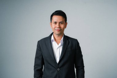 Asyalı iş adamı takım elbiseli, gri arka planda yalnız duran kamera stüdyosuna bakıyor. Genç Asyalı iş adamı yönetici ya da yönetici, gülümsüyor ve kendine güveni olması başarıyla olumlu..