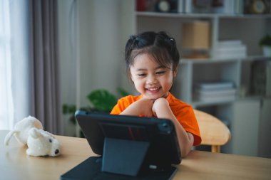 Asyalı kız tablet ekranı kullanıyor ve dokunuyor. Bebek gülümseme tableti kullanmak için komik bir zaman. Çok fazla ekran zamanı. TV ve internet bağımlılığı konsepti izlerken güzel bir kız video izliyor..