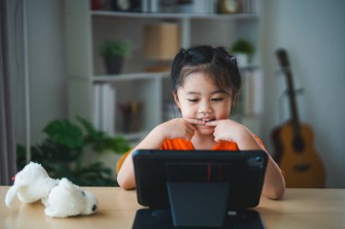 Asyalı kız tablet ekranı kullanıyor ve dokunuyor. Bebek gülümseme tableti kullanmak için komik bir zaman. Çok fazla ekran zamanı. TV ve internet bağımlılığı konsepti izlerken güzel bir kız video izliyor..
