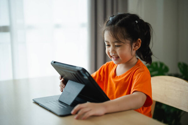 Asian child girl looking using and touch tablet display screen. Baby smiling funny time to use tablet. Too much screen time. Cute girl watching videos while tv, Internet addiction concept.