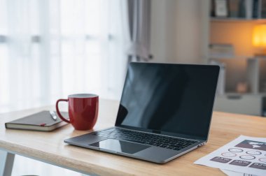 Laptop, çizelge dokümanları, kırmızı kahve fincanı, defter ve dekorasyonla çalışabilir çalışma odalarına yakından bakın. Oturma odası konseptinde ev işi..