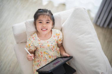 Tablet ekranında kalem ve dokunmatik resim kullanan Asyalı kız çocuğu. Bebek gülümseme tableti kullanmak için komik bir zaman. Çok fazla ekran zamanı. TV ve internet bağımlılığı konsepti izlerken güzel bir kız video izliyor..