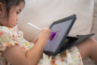 Tablet ekranında kalem ve dokunmatik resim kullanan Asyalı kız çocuğu. Bebek gülümseme tableti kullanmak için komik bir zaman. Çok fazla ekran zamanı. TV ve internet bağımlılığı konsepti izlerken güzel bir kız video izliyor..