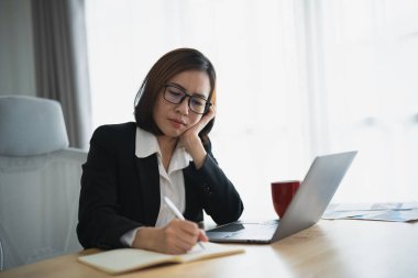 Siluet, ne yazık ki ciddi Asyalı iş kadını stresli depresyonda. Üzücü bir depresyon geçiriyor. Laptop üzerinde çalışıyor ve ofis masasının üzerine not defteri yazıyor. Bunalımlı kadın üzgün ciddi çalışıyor.